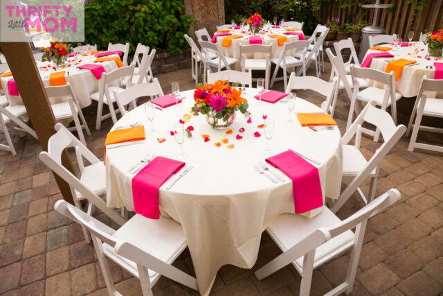 A round table with pink napkins and orange place settings.