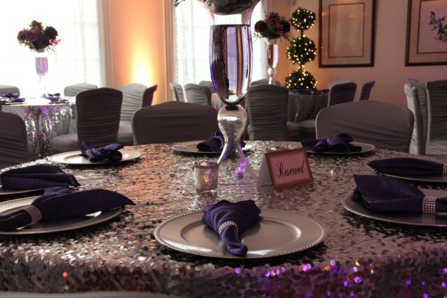 A table set with purple napkins and silver plates.